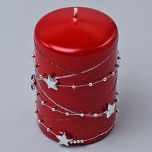 Červená sviečka s hviezdami a ozdobným reťazcom.