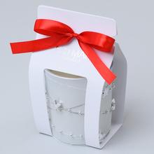 Biela voňavá sviečka v sklenenom obale s červenou stuhou.