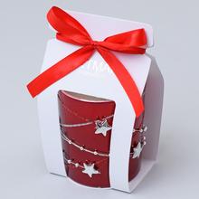 Červená voňavá sviečka v skle s ozdobným stužkovým uzáverom.