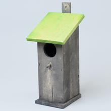 Sivá zahnietzďovacia budka so zelenou strechou.