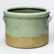 Zelený keramický obal s hladkým povrchom a hnedým spodkom.