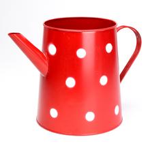 Červená kovová váza s veľkými bielymi bodkami.