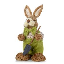 Hnedý zajac v zelenom oblečení s lopatou a slamou.