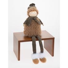 Textilná dekorácia chlapca sediaceho v hnedo-béžových farbách.