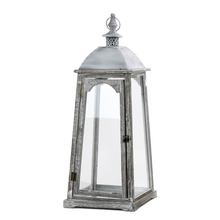 Šedobiely lampáš s priehľadným sklom a kovovým vrchom.