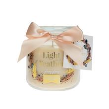 Malá béžová sviečka v skle s ozdobnou stuhou.