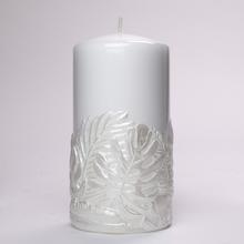 Biela sviečka s dekoráciou listov monstera.