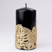Čierna sviečka s dekoráciou z listov monstera.
