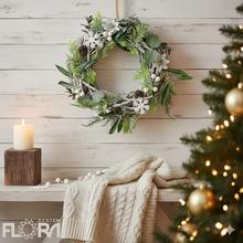 Vianočný veniec z prútia so zelenými a bielymi dekoráciami.