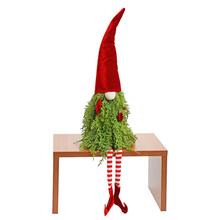 Škriatok sediaci v červenom a zelenom oblečení s dlhým červeným klobúkom.